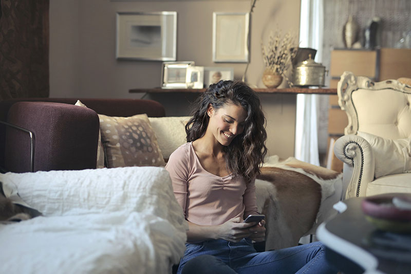 une femme utilisant son smartphone compatible esim dans son salon et profitant d'un deuxième numéro